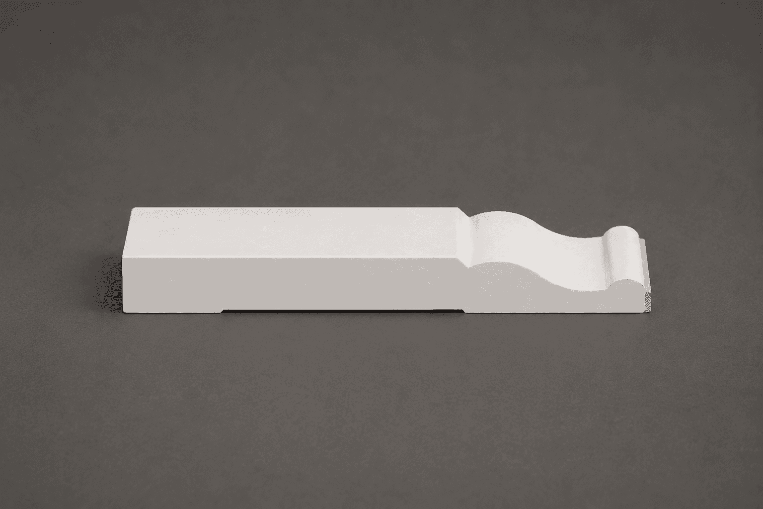 Primed white baseboard moulding lying on its back, showing the cove and bead profile along its top edge