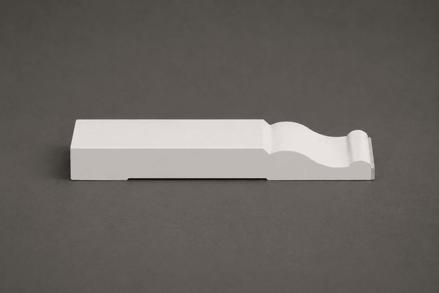 Primed white baseboard moulding lying on its back, showing the cove and bead profile along its top edge