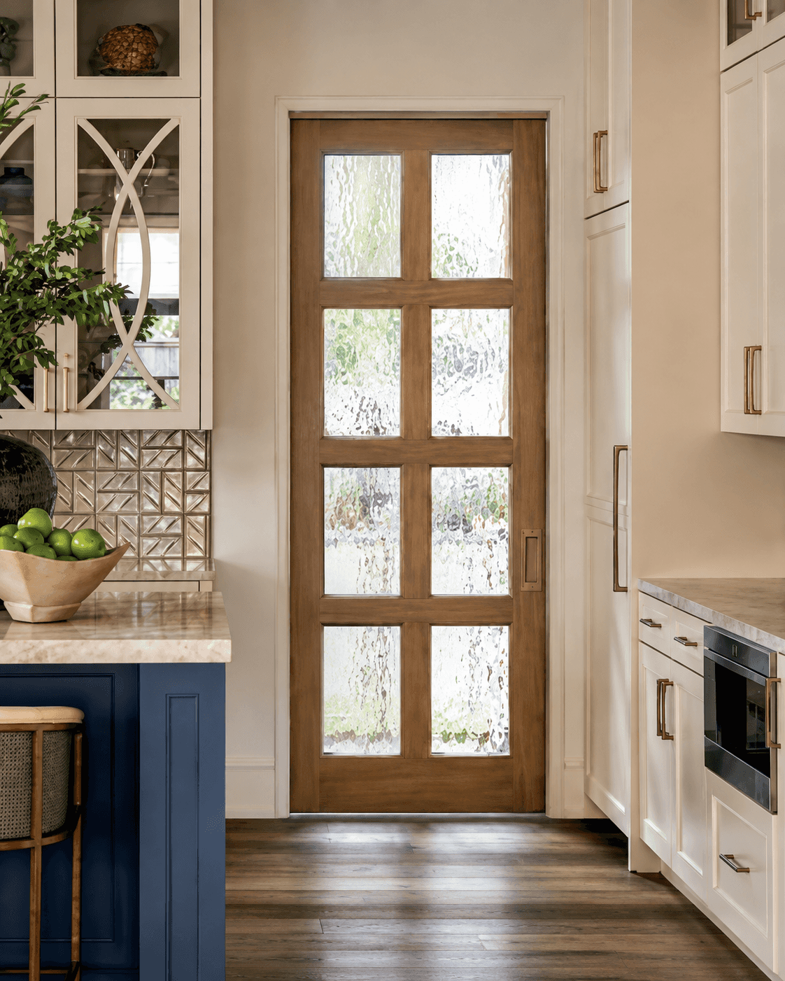 Stained wood door with eight textured glass panels, set between white cabinets in a kitchen