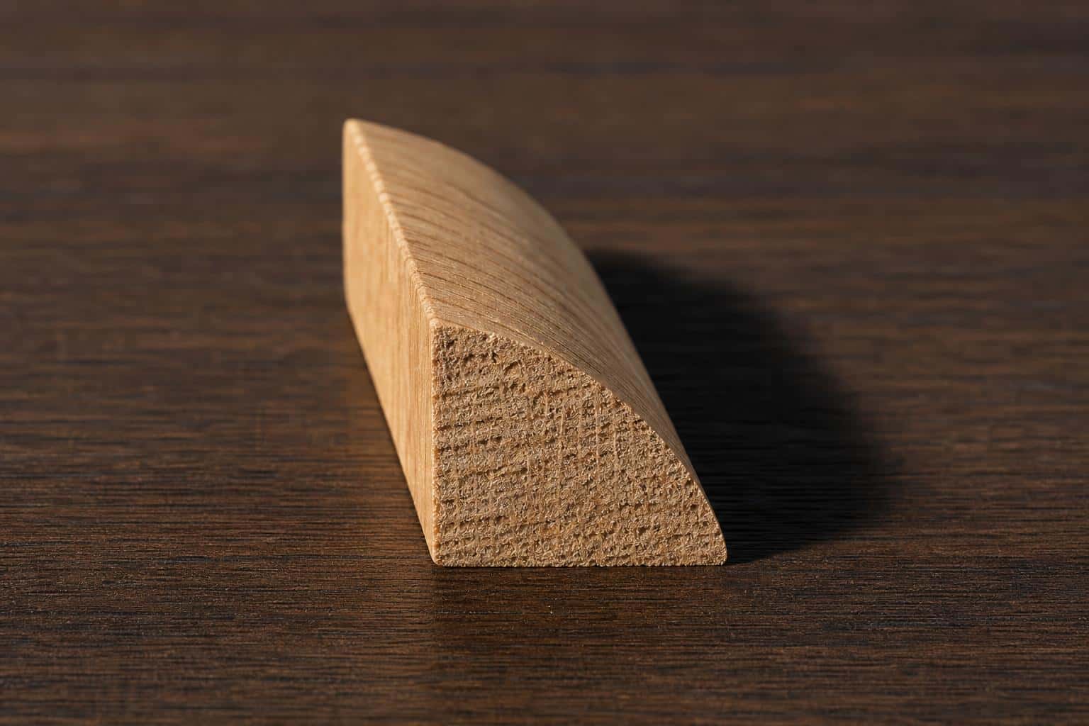 Short piece of unfinished oak quarter round seen end-on, showing its quarter-circle profile