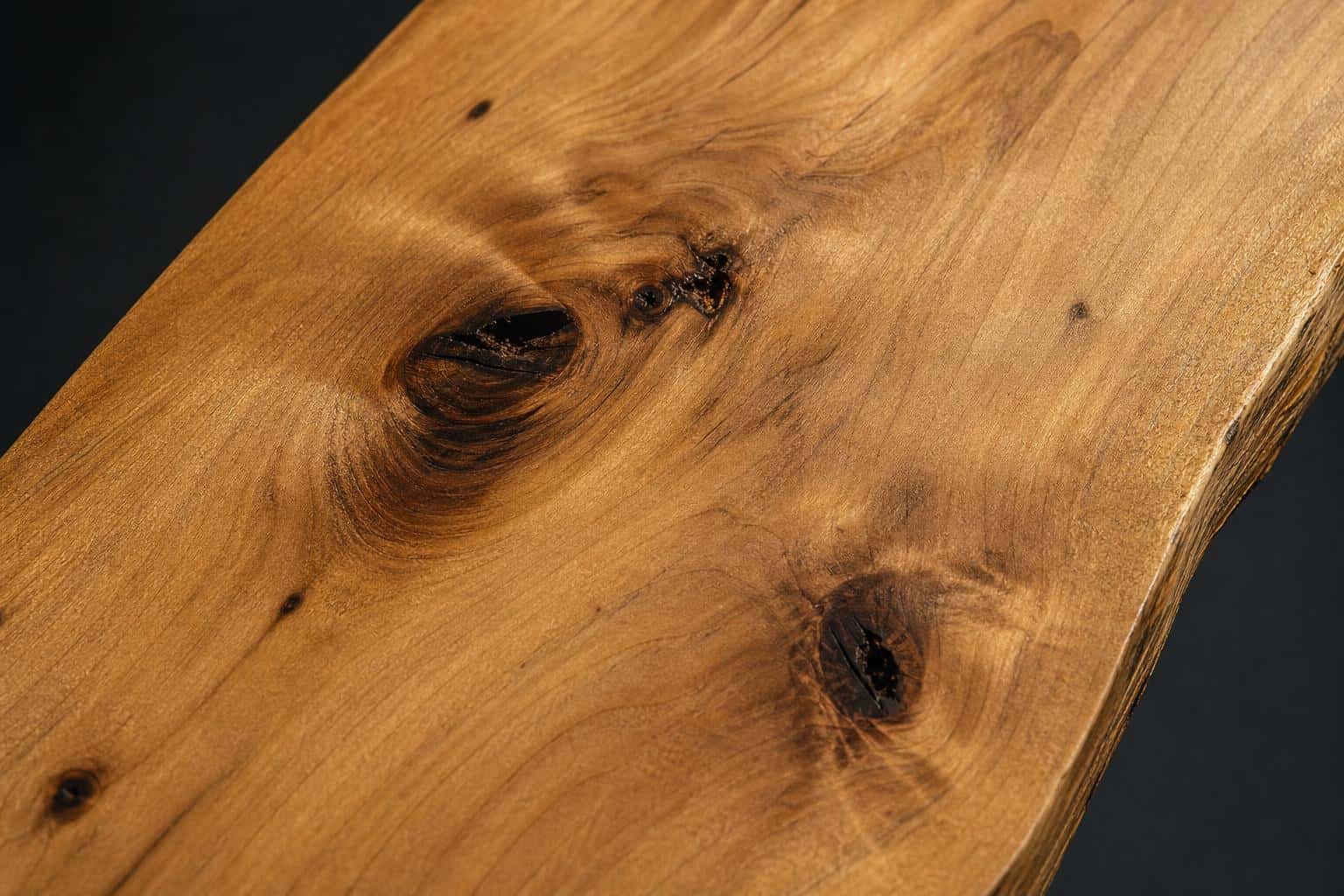 Knotty alder board with a honey-brown face, dark knots and an uneven natural edge, close-up