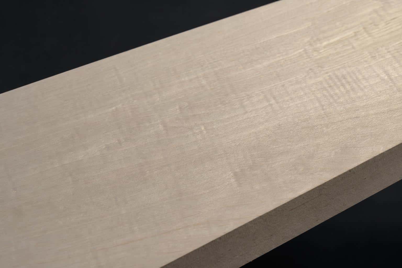 Soft maple board with a pale, creamy face and a light ripple in the grain, close-up of the face and edge