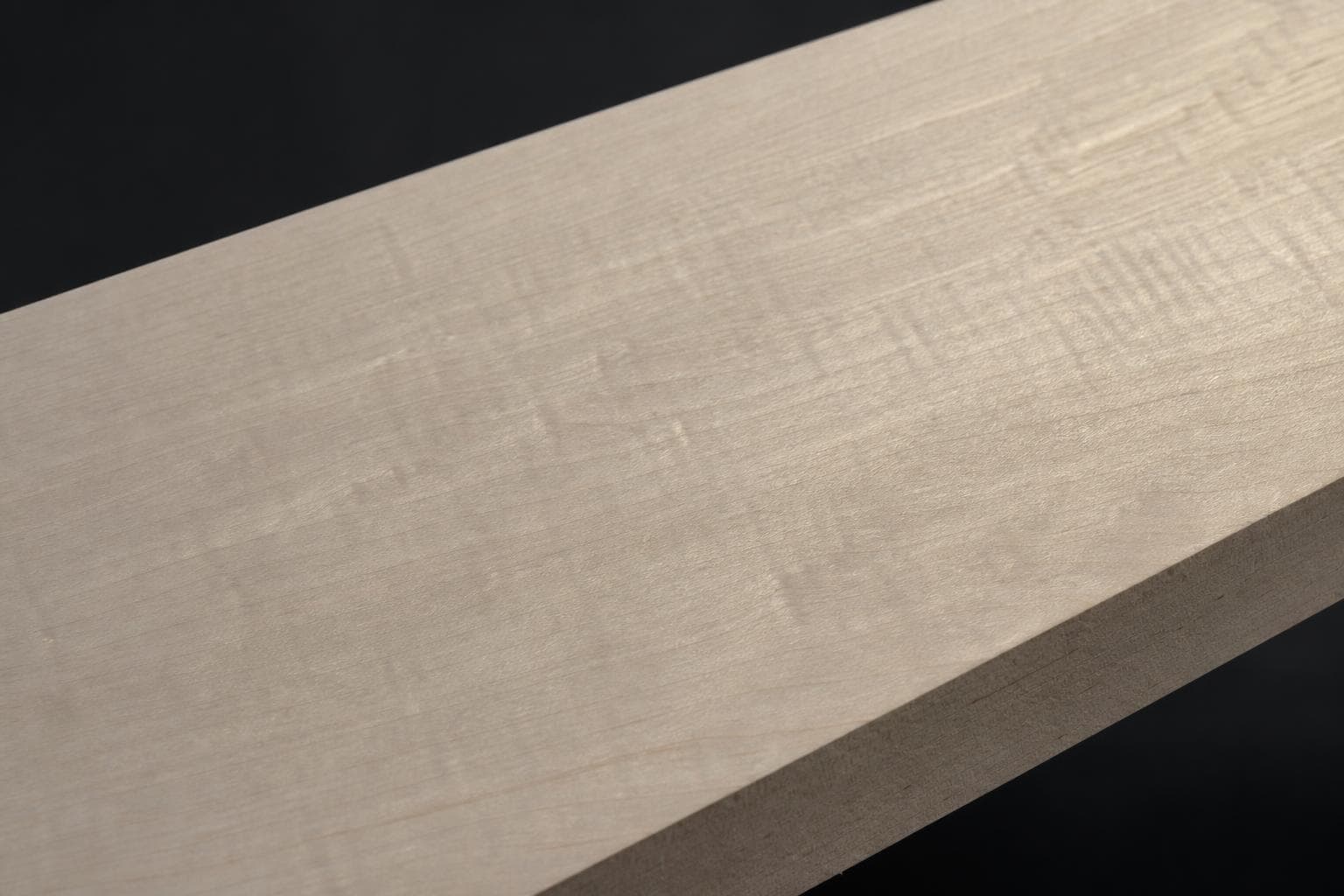 Soft maple board with a pale, creamy face and a light ripple in the grain, close-up of the face and edge