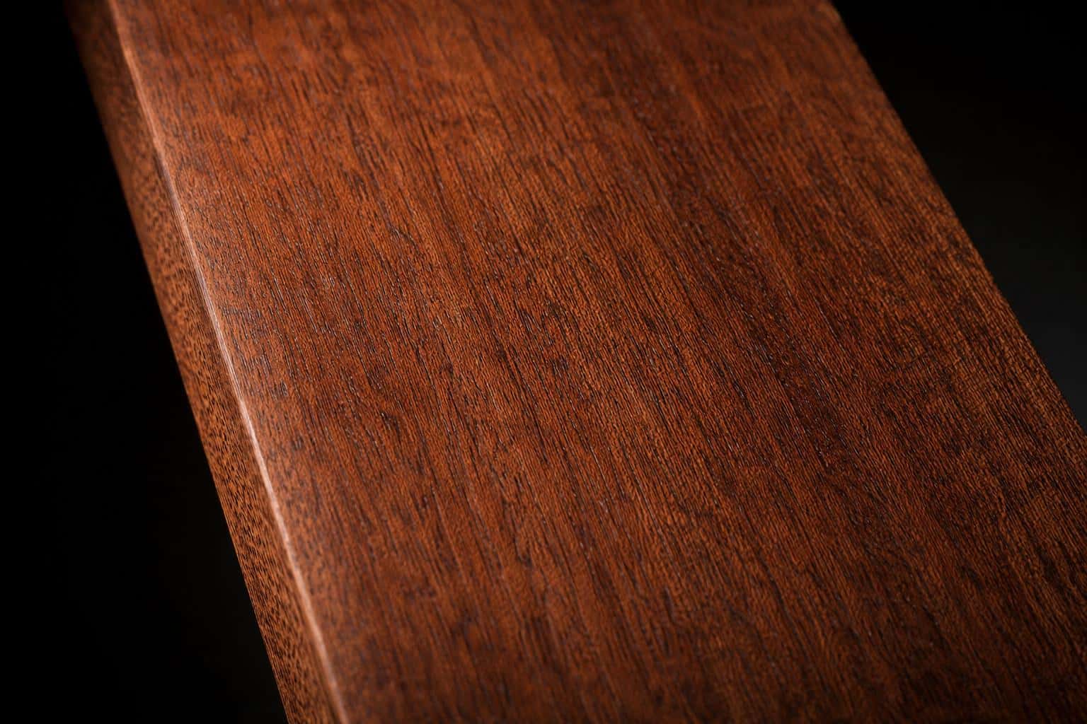 Genuine mahogany board with a reddish-brown face and fine, straight grain, close-up of the face and edge
