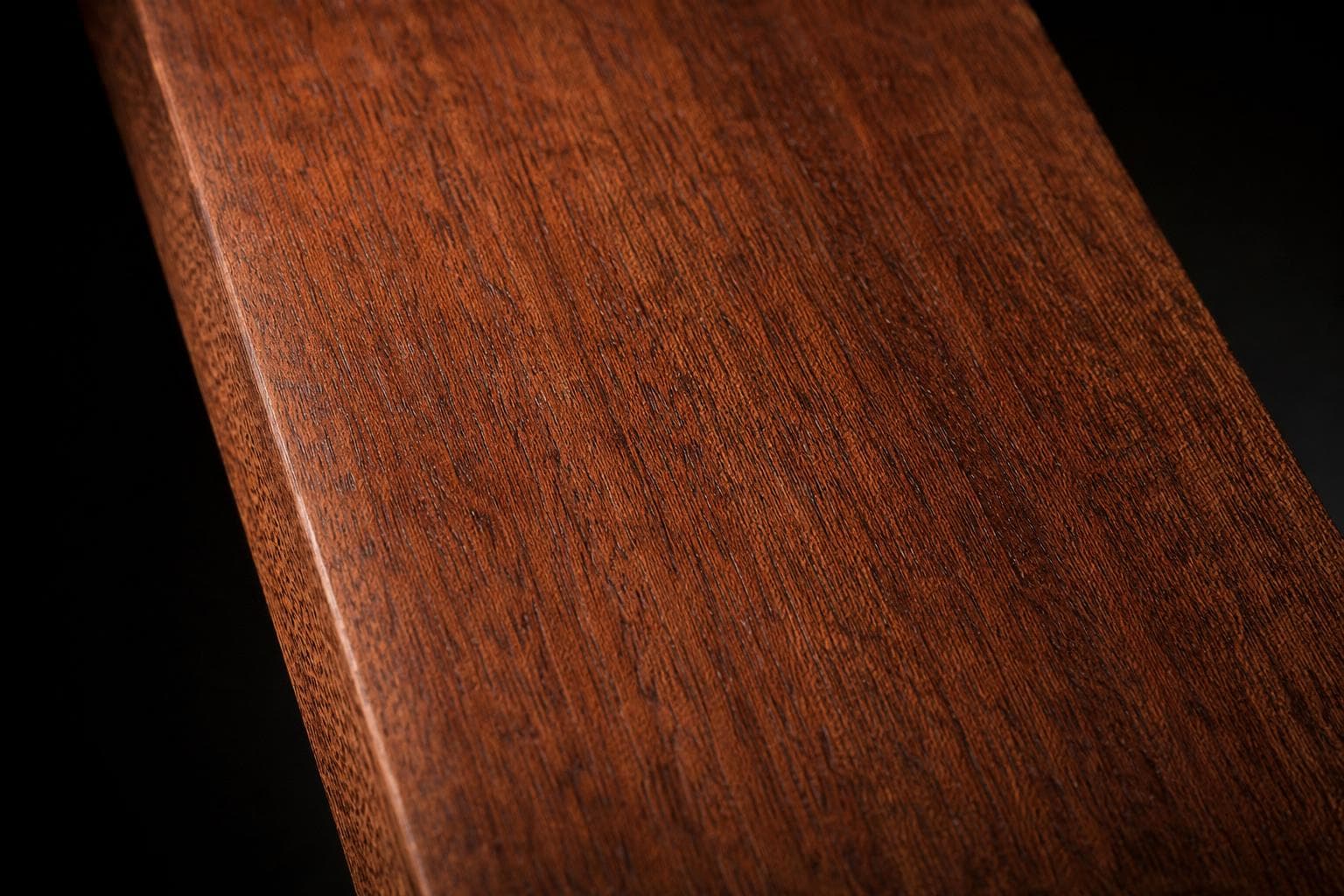 Genuine mahogany board with a reddish-brown face and fine, straight grain, close-up of the face and edge