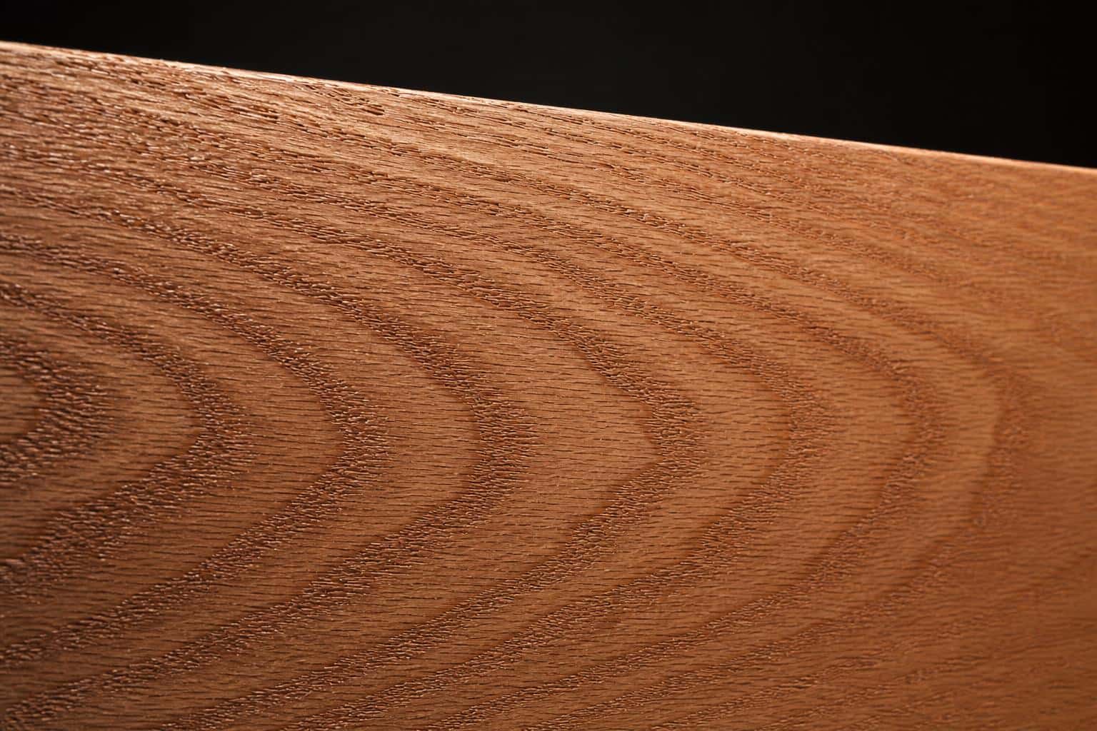 Red oak board with a warm pinkish-brown face and bold cathedral grain, close-up