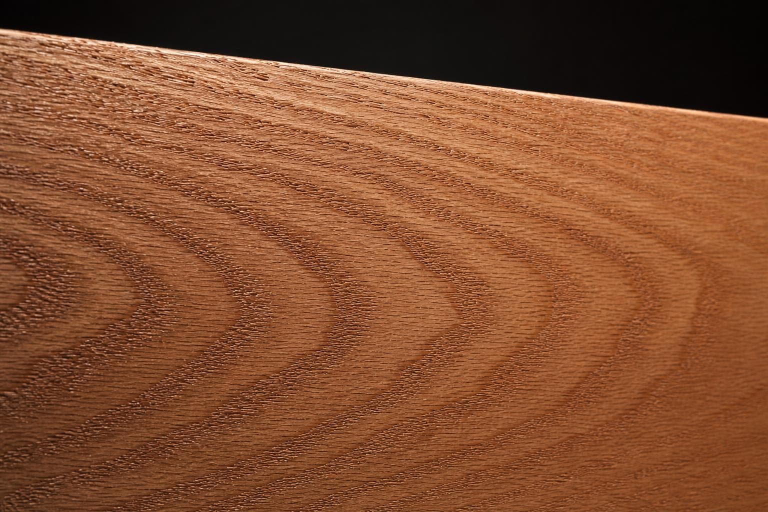 Red oak board with a warm pinkish-brown face and bold cathedral grain, close-up