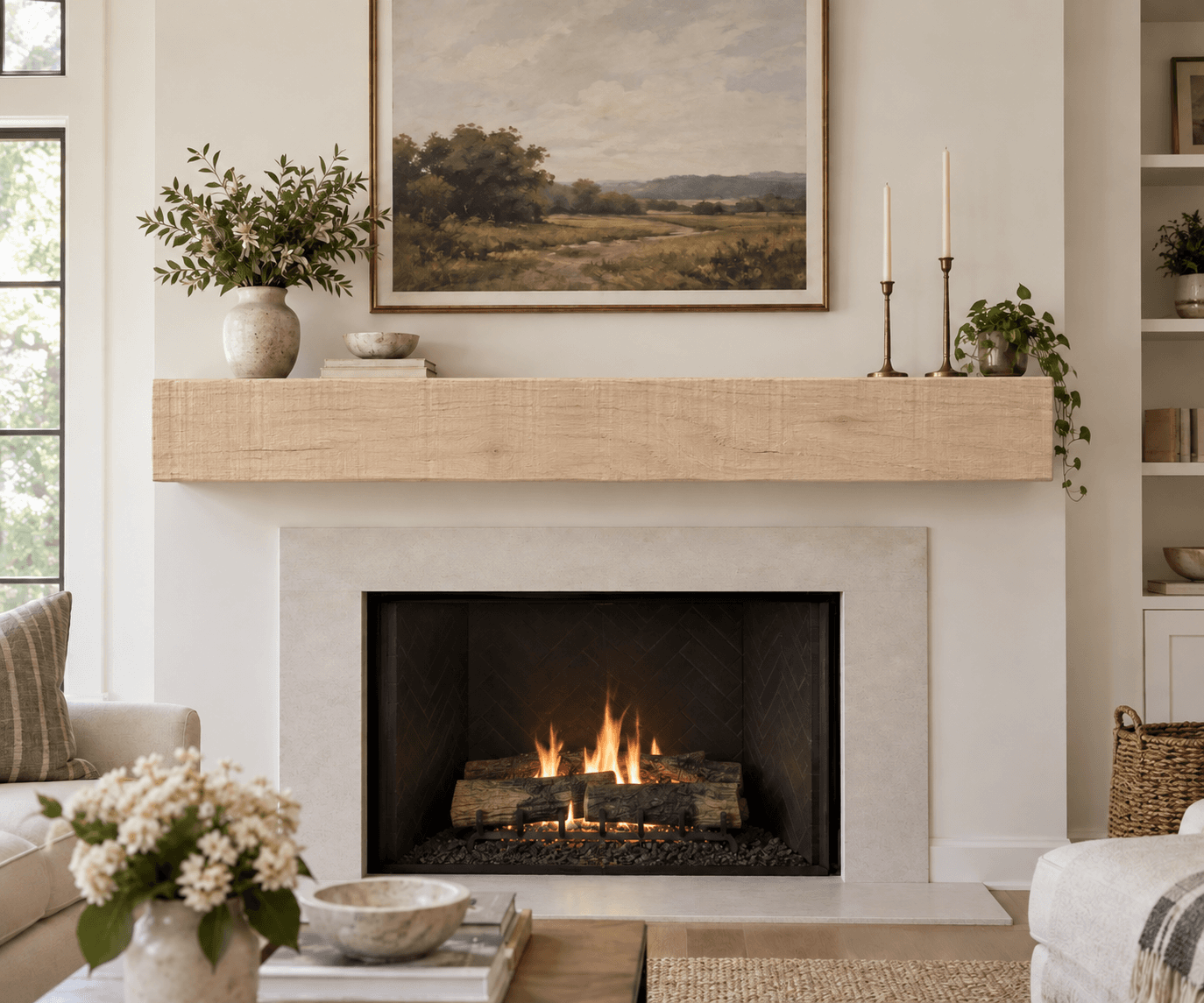 Light rough-sawn box mantel above a lit fireplace, with candlesticks and a landscape painting on top